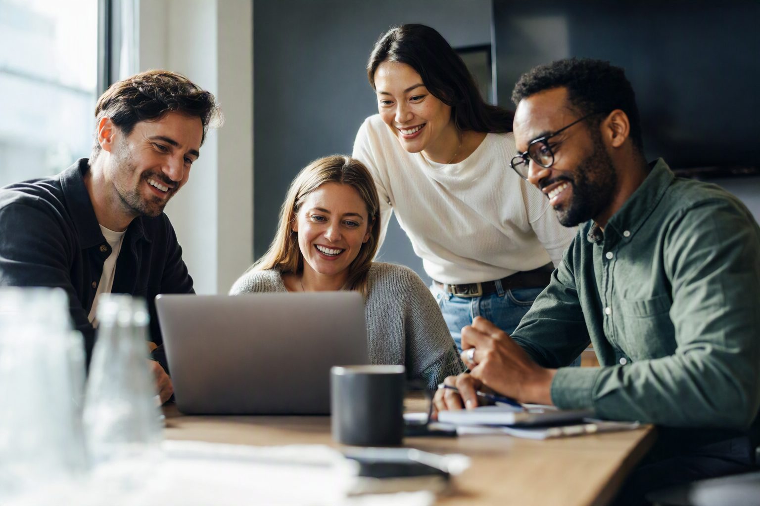 Four coworkers smiling as they look at a laptop together